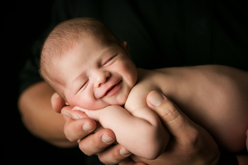 Smiling newborn baby cradled in their fathers hands